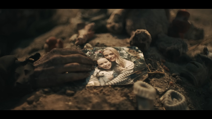 A hand rests on a photograph of a woman and child, surrounded by rubble.