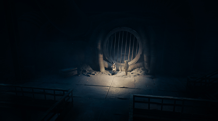 The two characters stand before a large barred circular door in a dark underground chamber.