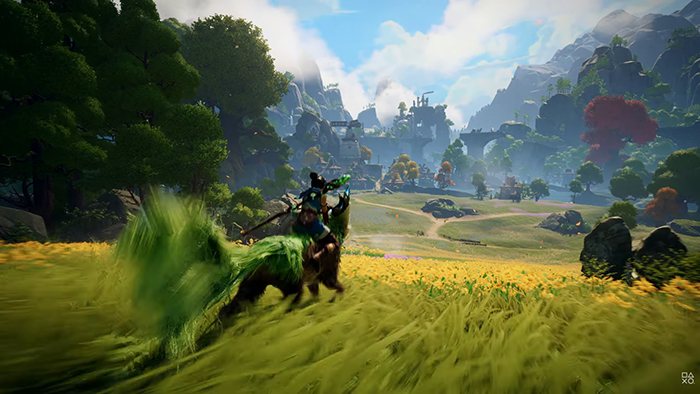 Kena rides a large, fox-like spirit companion across a vibrant meadow filled with yellow flowers. Rolling hills, ancient ruins, and distant mountains stretch into the horizon under a bright blue sky.