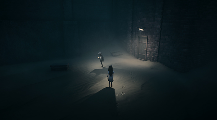 Inside a dark stone chamber, the two characters stand beneath a single overhead light.