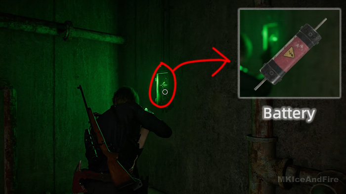 In a dark corridor lit by green emergency lights, the character picks up a red Battery from a wall-mounted slot.