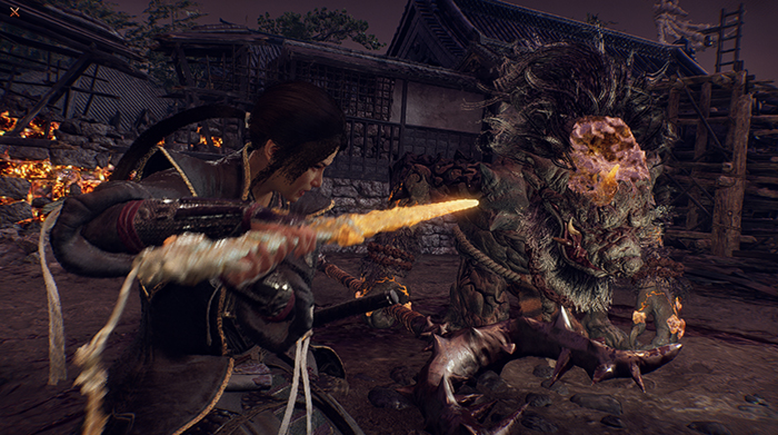Nioh 3 combat scene showing the protagonist using a flaming weapon to attack a large monster in a village setting.