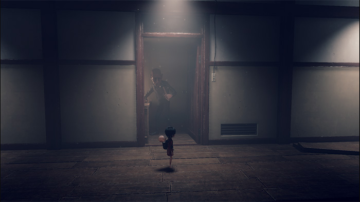 A young girl character, carrying a baby on her back, stands in a dimly lit traditional Japanese-style room. In the doorway ahead, a tall, eerie man with dark clothing and an unsettling expression watches her. The scene is quiet and tense, with soft light filtering through the door.