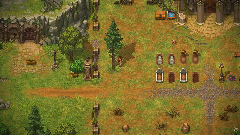 Top-down view of a cemetery area in Graveyard Keeper II: multiple grave markers (some ornate, some simple), stone crosses, an arched tomb entrance, and scattered bones. A character walks near a tree, with a chest and water basin nearby. Cobblestone paths intersect grassy terrain under soft daylight.