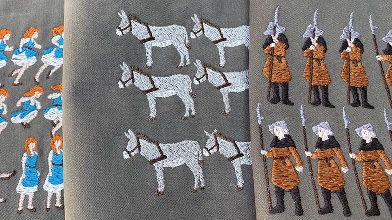 Close-up of embroidered fabric: female protagonist's animation frames on the left, donkey's animation frames in the middle, and guard NPC's pose frames on the right, all set against a grey linen background.