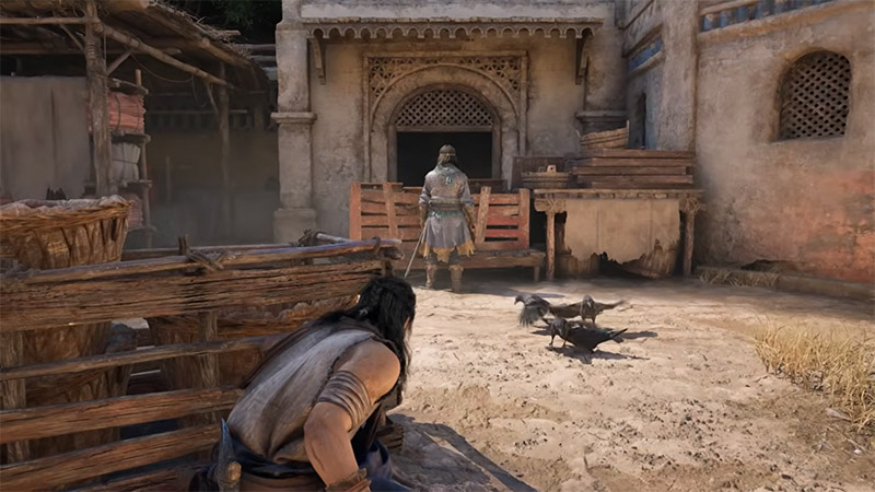 The protagonist crouches behind wooden crates, observing from cover; three crows gather on the sandy ground, while a guard stands in the arched doorway ahead.