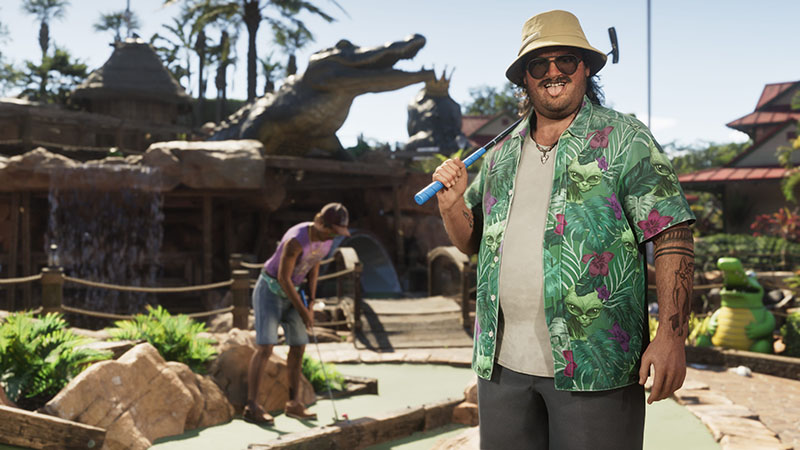 GTA6 Cal Hampton standing on a mini-golf course—wearing a beige bucket hat, sunglasses, patterned green Hawaiian shirt over a white tee, and dark pants; holding a blue putter. In background: another player putting, tropical decor, rock formations, and a large crocodile sculpture.