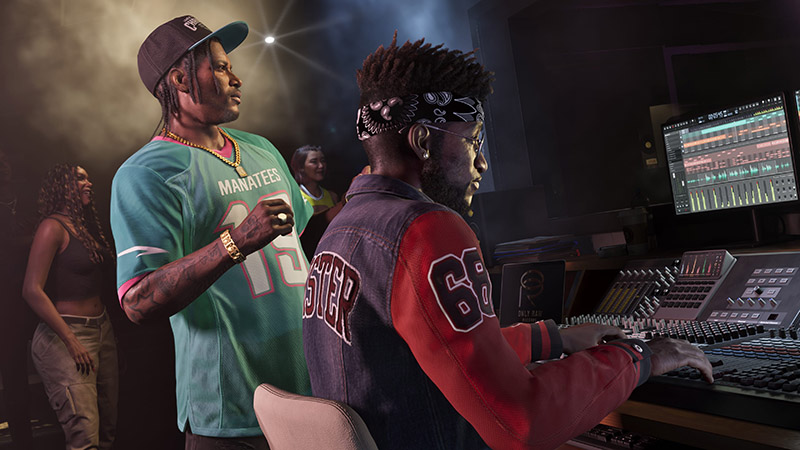 GTA6 Dre’Quan Priest seated at a professional audio mixing console—wearing a denim-and-red varsity jacket with “68” on the sleeve and “STER” (partial) on the back, a bandana, glasses, and earpiece; hands actively adjusting faders. To his left: another man in a teal “MANATEES” jersey and cap, holding a cup.