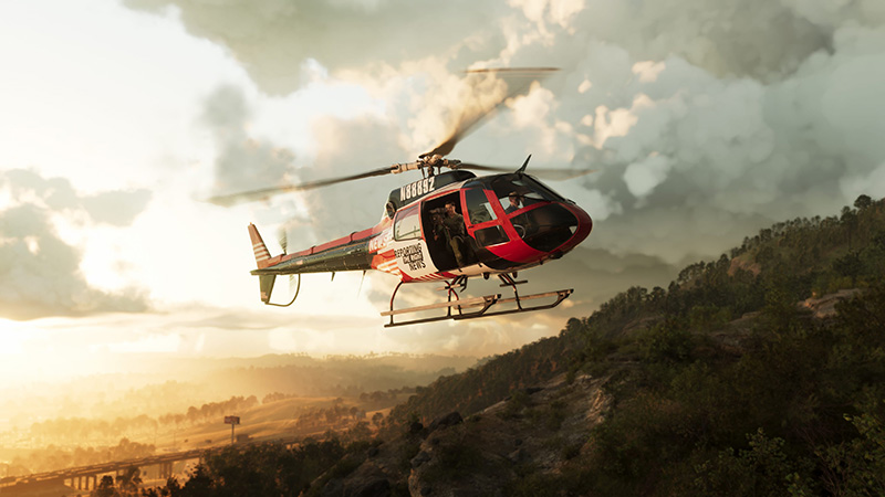 GTA6 official scene: A red-and-white Bell 206-style helicopter with open side door and visible registration N9488Z flies low over a forested hillside at golden hour, with sunlit haze, distant highway, and rolling terrain below.